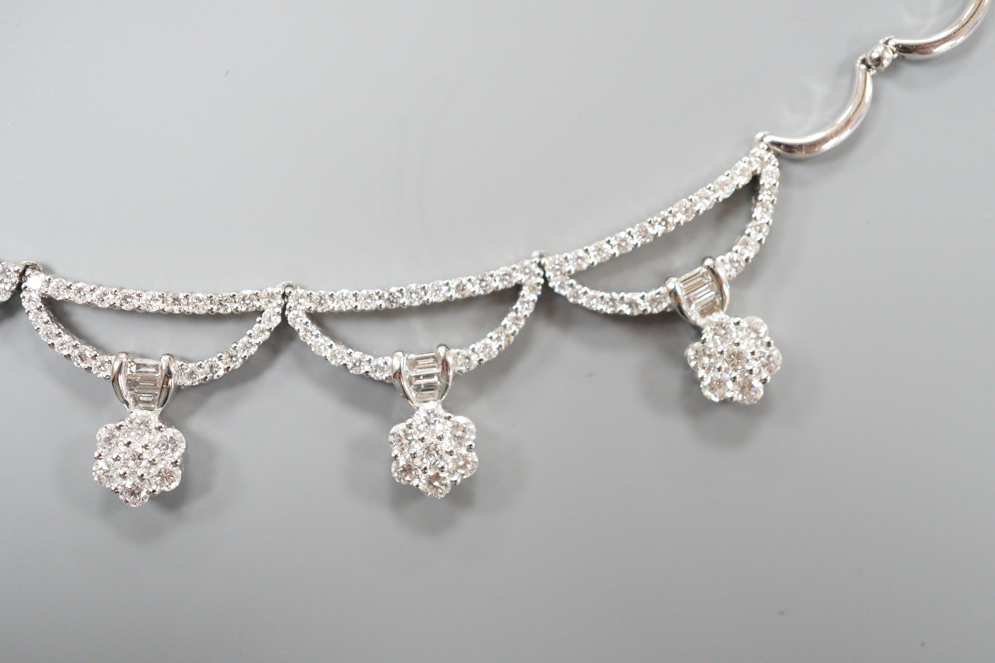 A modern 750 white metal and septuple baguette and round cut diamond cluster set curved link fringe necklace, 43cm, gross weight 26.6 grams